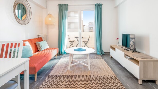 A modern living room with a sofa, a dining table, and a TV. - Appartement Corail - Welkeys (Antibes)
