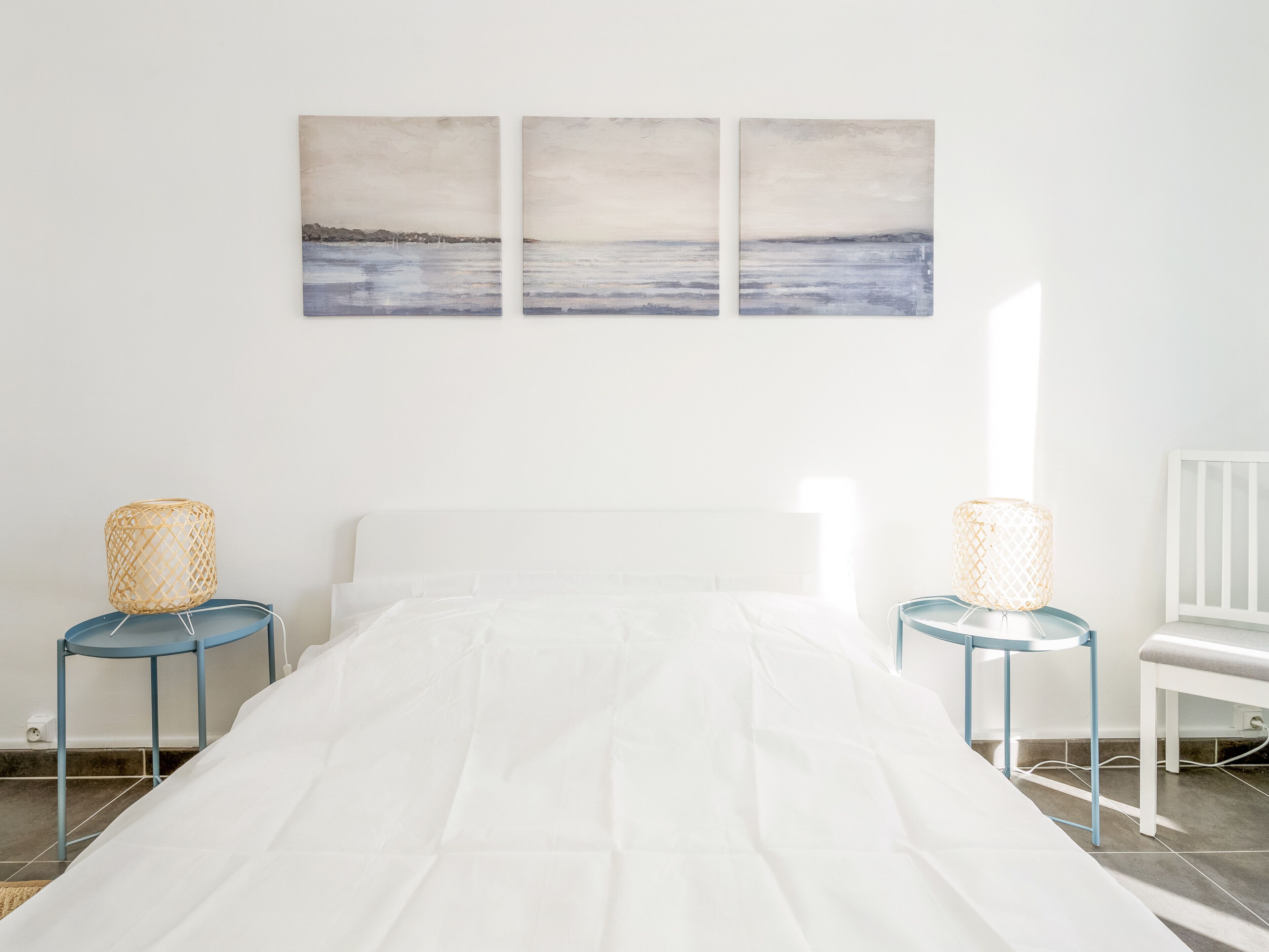A bedroom with a bed, two nightstands, a chair, and three wall-mounted paintings.
