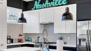 Una cocina moderna con una isla grande, taburetes de bar, un letrero de neón y electrodomésticos de acero inoxidable.