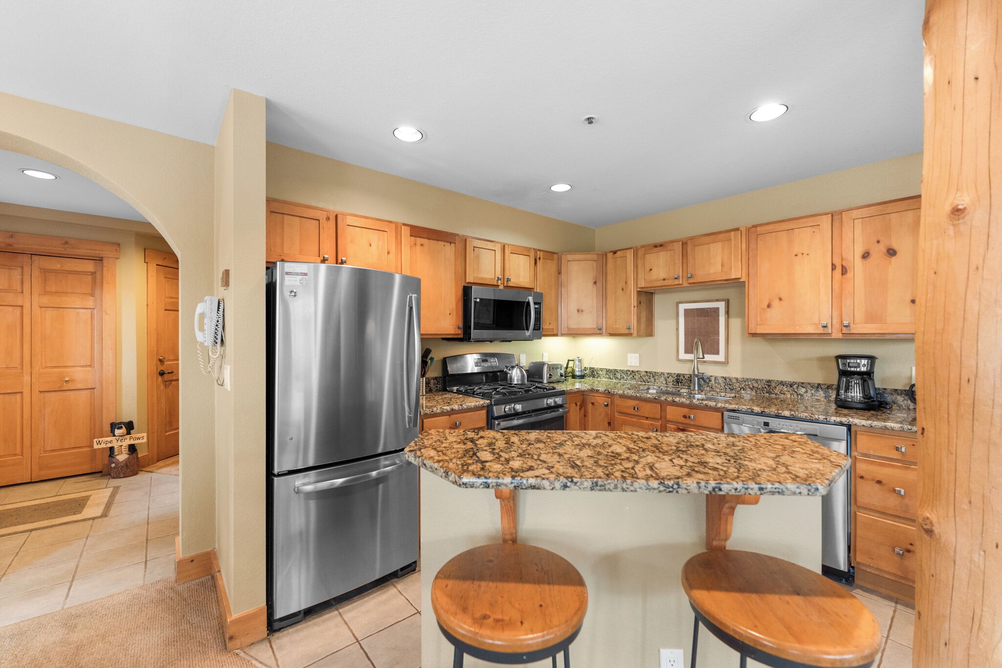 A kitchen with wooden cabinets, stainless steel appliances, granite countertops, and a central island with stools.