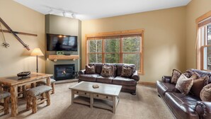 A cozy living room with a fireplace, a television, a large window, and a leather couch. - Trapper's Crossing #8761 by Summit County Mountain Retreats (Keystone)