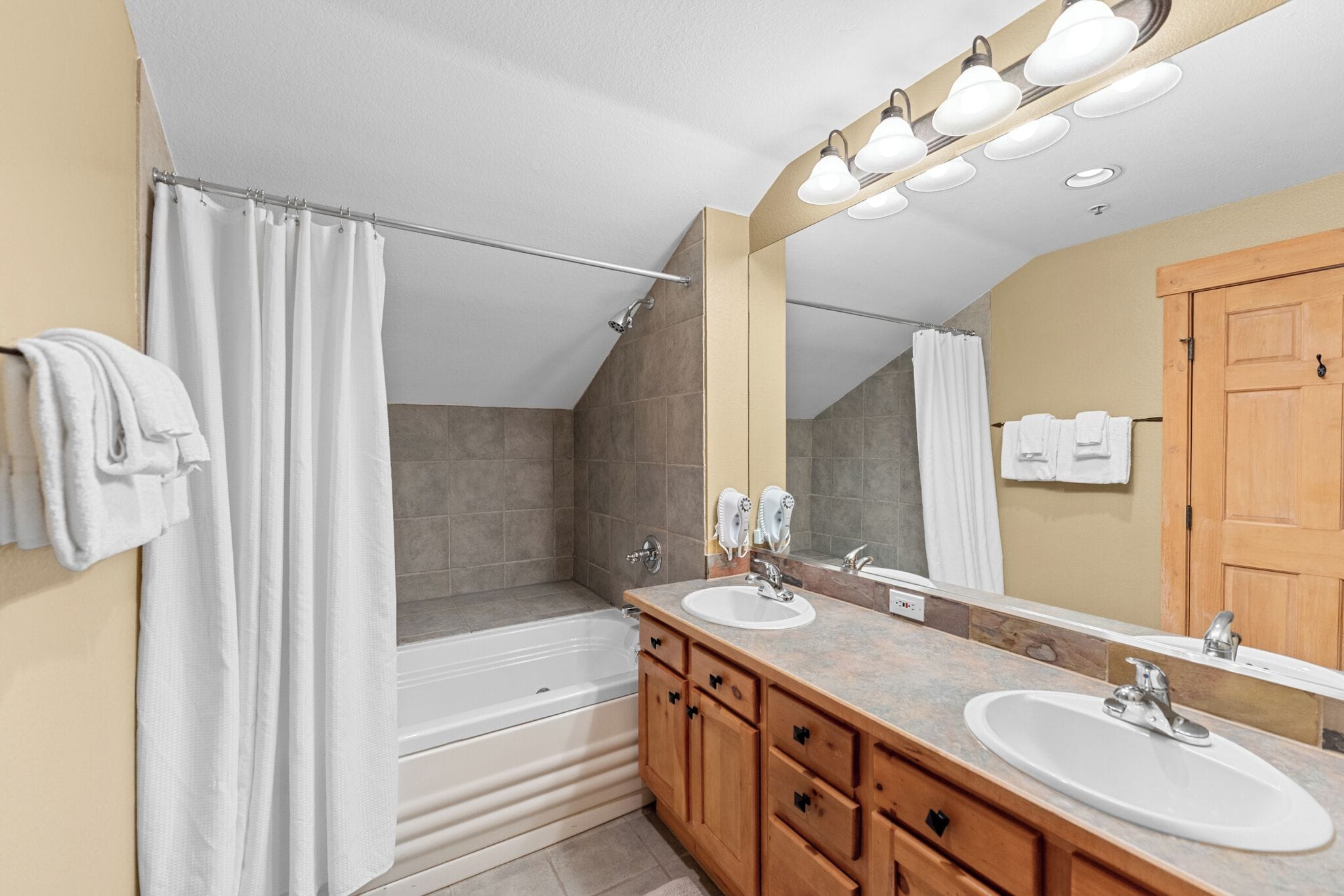 A modern bathroom with a bathtub, two sinks, a large mirror, and a shower curtain.