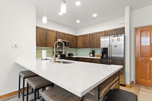 Une cuisine moderne dotée d’un grand îlot central, d’appareils électroménagers en acier inoxydable, de meubles de rangement en bois et d’un four à micro-ondes encastré.