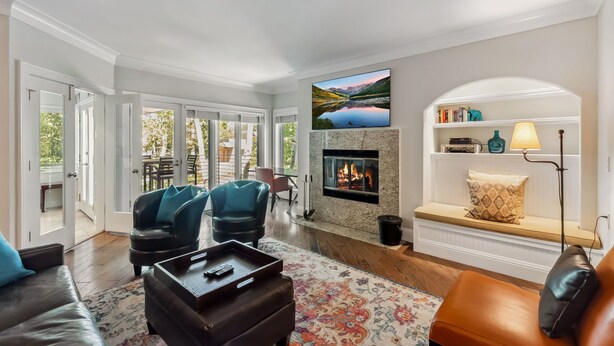 Una sala de estar con chimenea, televisor montado encima y vistas a un lago a través de las ventanas.