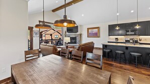 A spacious dining area with a wooden table and chairs, a bar with stools, and a kitchen with dark cabinets and a large island. - Alders #8 by Summit County Mountain Retreats (Keystone)