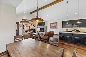 A spacious dining area with a large wooden table and chairs, a bar area with stools, and a kitchen with dark cabinets and modern appliances. - Alders #8 by Summit County Mountain Retreats (Keystone)