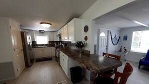A kitchen with white cabinets, a granite countertop, and a dining area with wooden chairs. - 3 MIN FROM PRIVATE BEACH & BOAT RAMP (Key Largo)