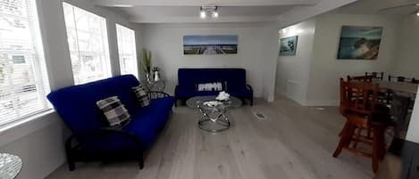 Ett vardagsrum med en blå soffa, ett runt soffbord och en matplats med stolar i trä.