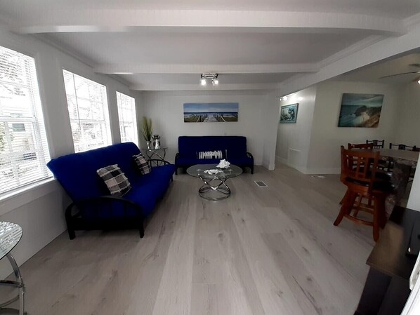 Ein Wohnzimmer mit blauem Sofa, einem runden Couchtisch und einem Essbereich mit Holzkohlen.