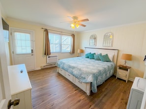 A bedroom with a bed, a ceiling fan, a window with curtains, a heater, and a nightstand with a lamp.