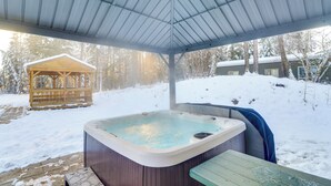 A covered outdoor hot tub area with a wooden deck, a wooden gazebo, and a house in the background. - Columbia Falls Private Retreat: Pool Table & Deck! (Columbia Falls)