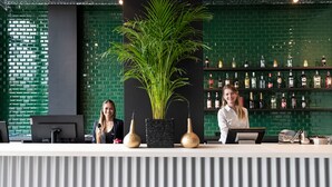 A reception area with a green brick wall, a large potted plant, and a bar stocked with various bottles. - B&B Hotel Oftringen (Oftringen)