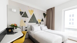 A hotel room with a bed, a desk with a laptop, a chair, and a wall with geometric patterns. - B&B Hotel Oftringen (Oftringen)
