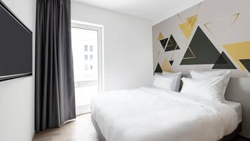 A modern hotel room with a large bed, a window with curtains, and a geometric wall design.
