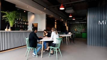 A modern cafe with a bar area, green chairs, and a mix of natural and industrial decor.