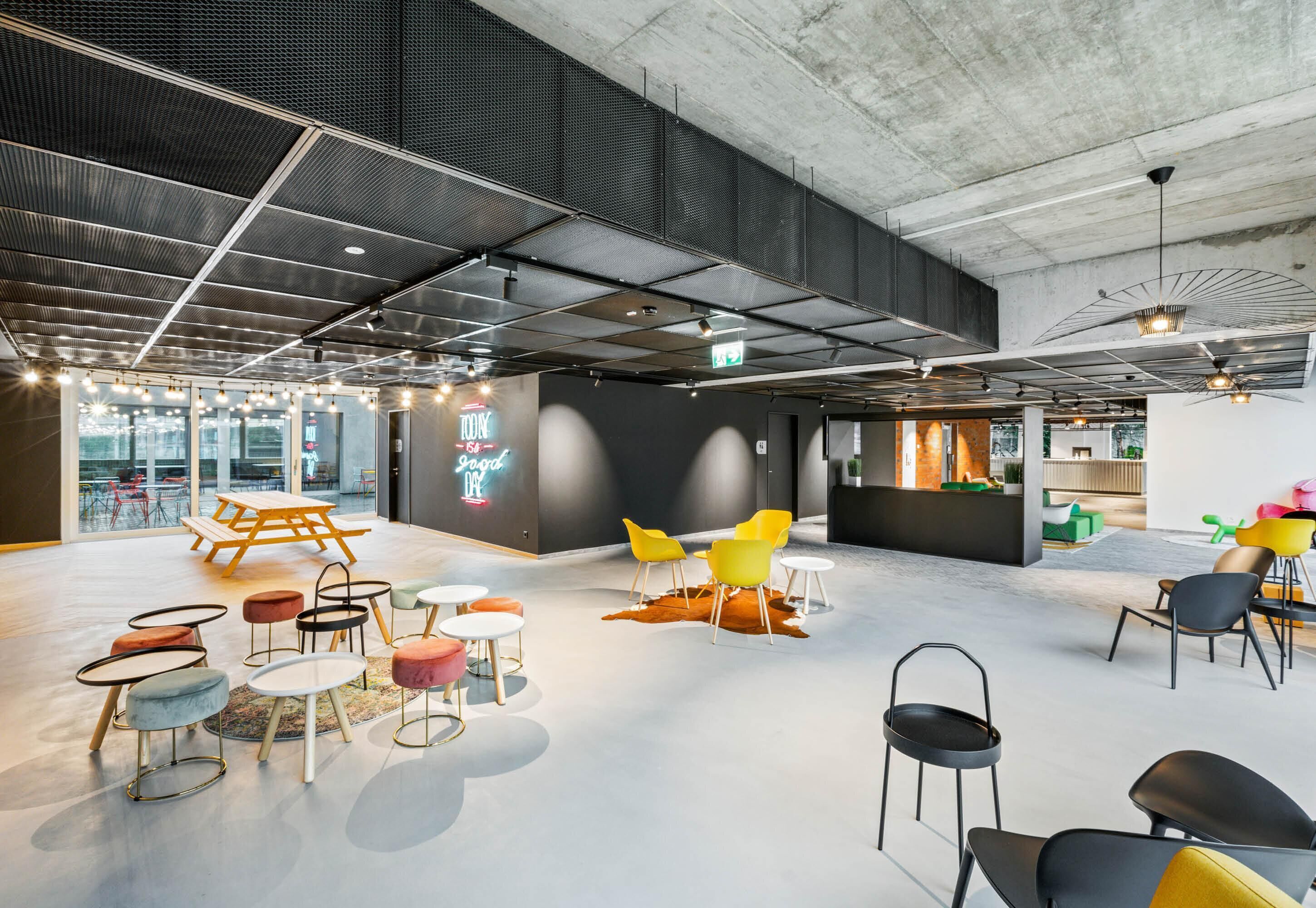 Un espacio interior moderno con techo de concreto, varias zonas de estar y una señal de salida visible.