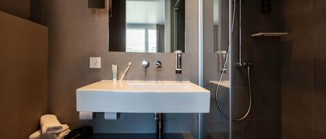 A modern bathroom with a white sink, a mirror, a shower, and a towel rack.