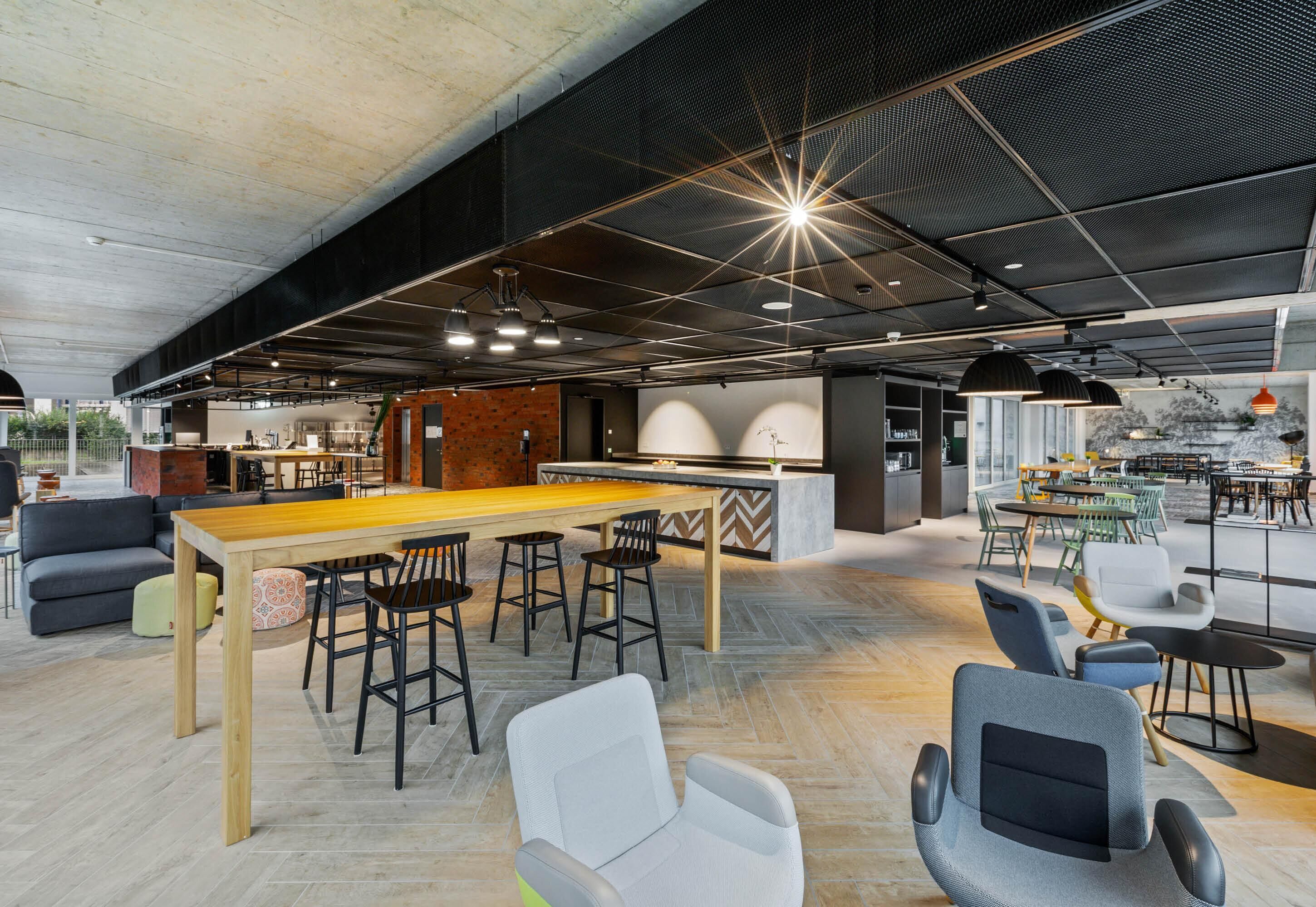 A modern interior with a long wooden table, bar stools, and various seating options.