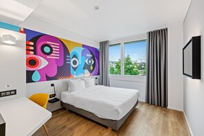 Una habitación de hotel moderna con una cama grande, un escritorio y un mural abstracto y colorido en la pared.