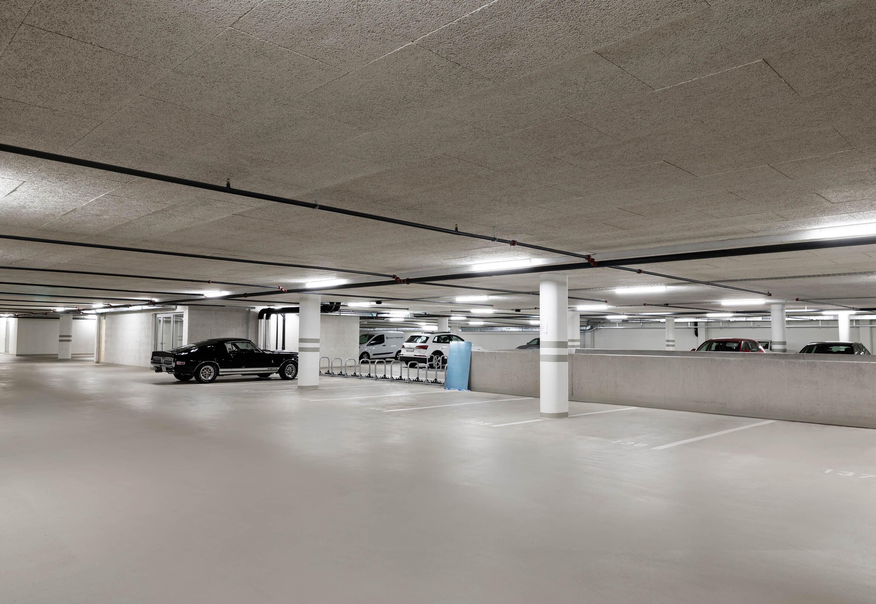 Eine Tiefgarage mit Betonpfeilern, Neonbeleuchtung und mehreren parkenden Autos.