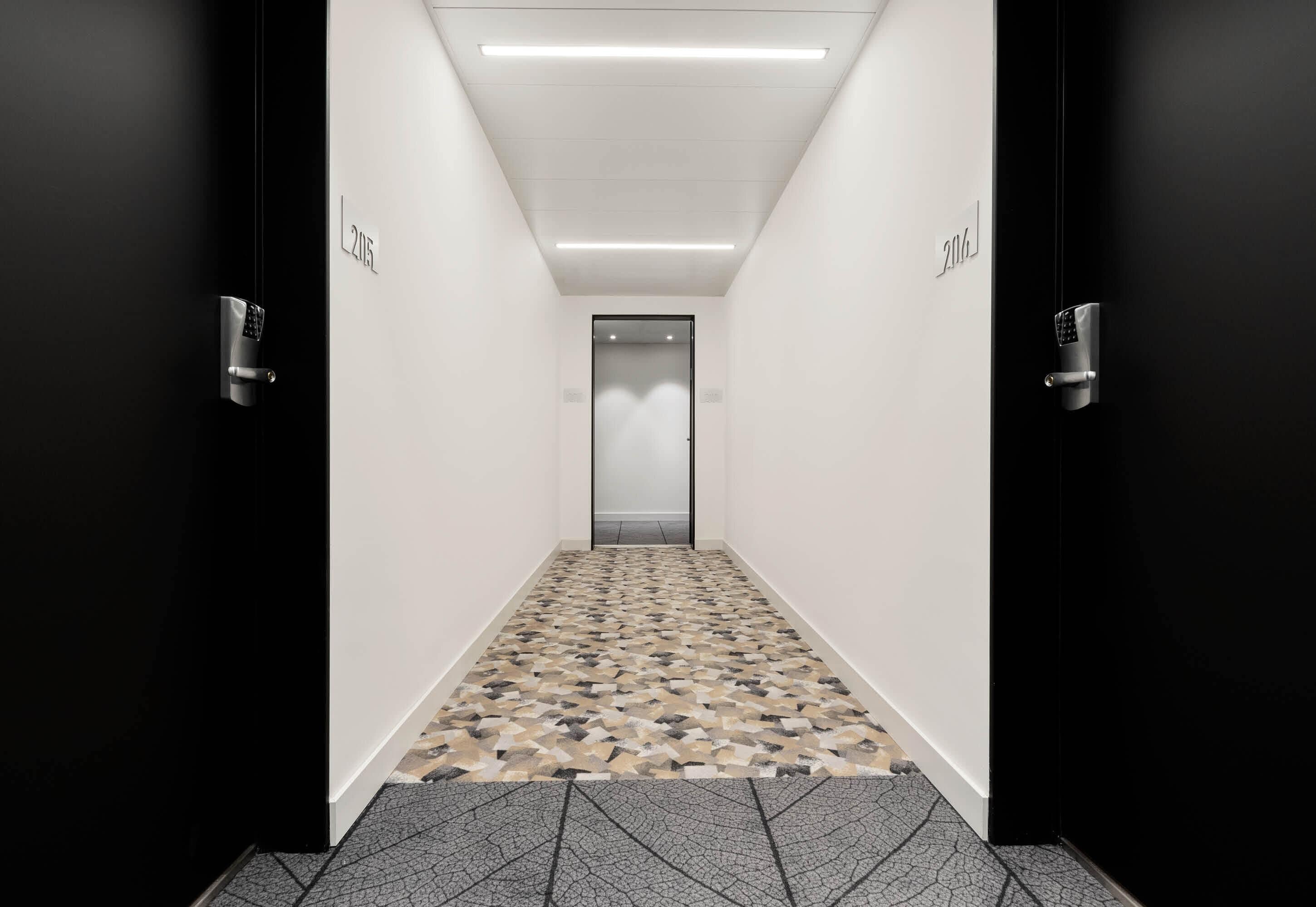 A hallway with a patterned floor, a modern elevator, and doors labeled 'L216'.