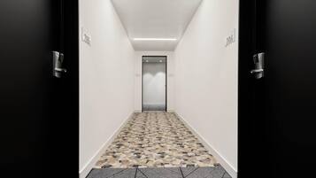 A hallway with a patterned floor, a modern elevator, and doors labeled 'L216'.
