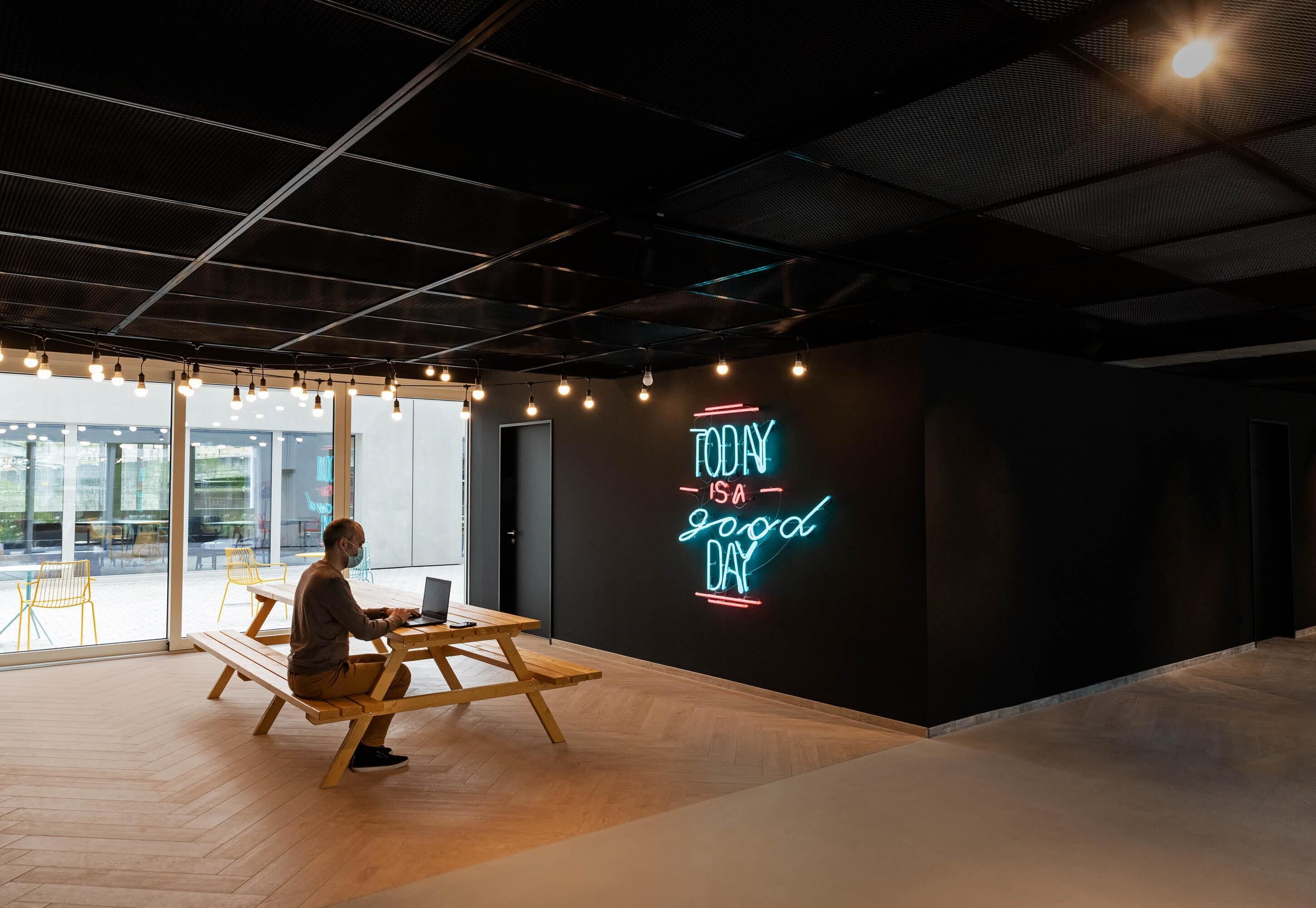 Ein modernes Interieur mit einer Neonreklame, Holzbanken und einem großen Fenster.