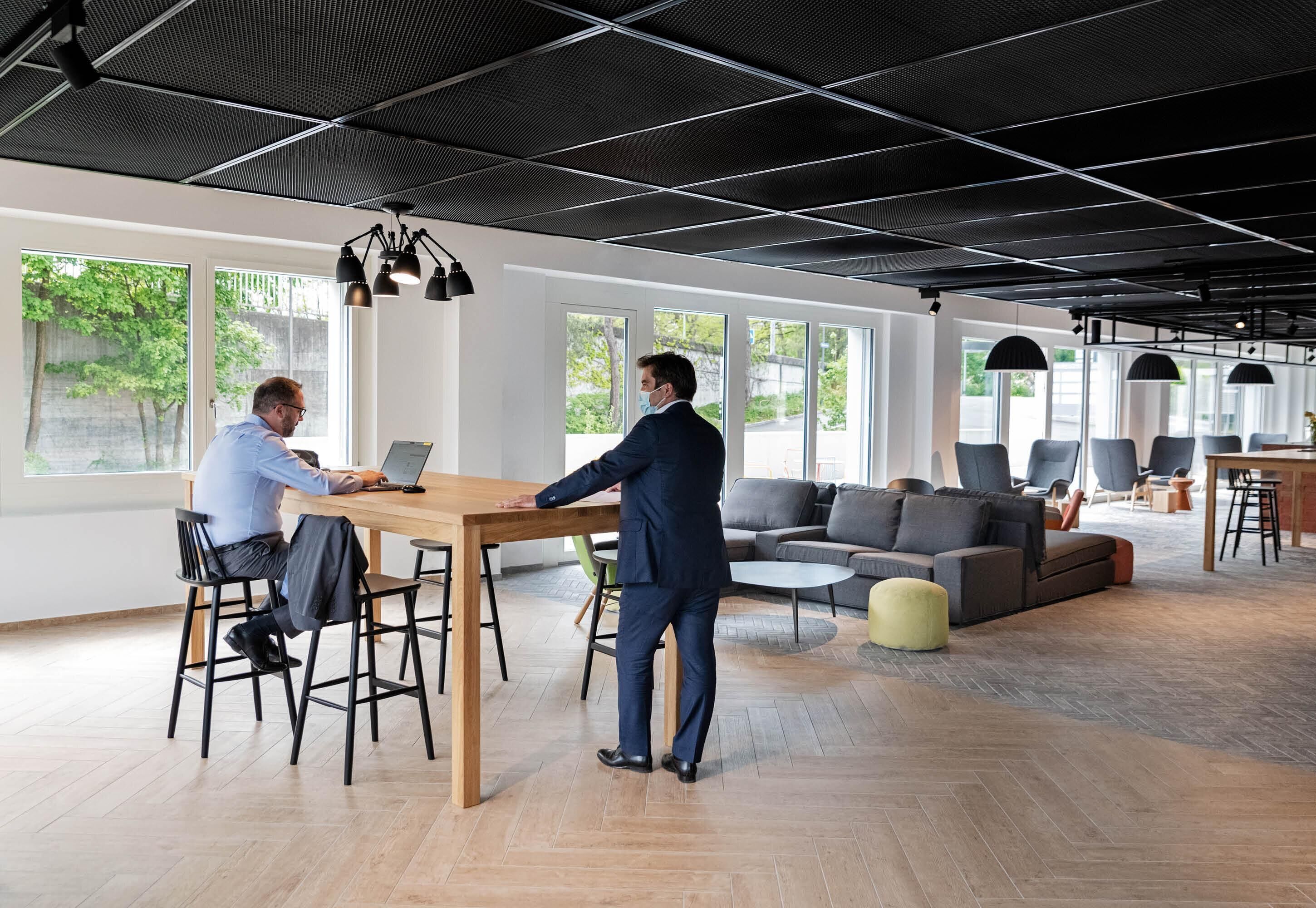 A modern office space with a large table, multiple chairs, a sofa, and a dining area.