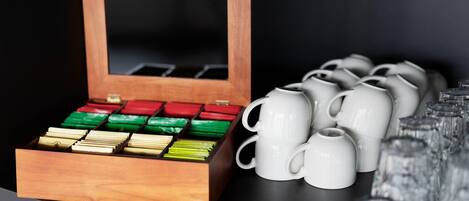 Una caja de madera con compartimentos que contienen diversos objetos, tazas blancas y una fila de vasos transparentes.