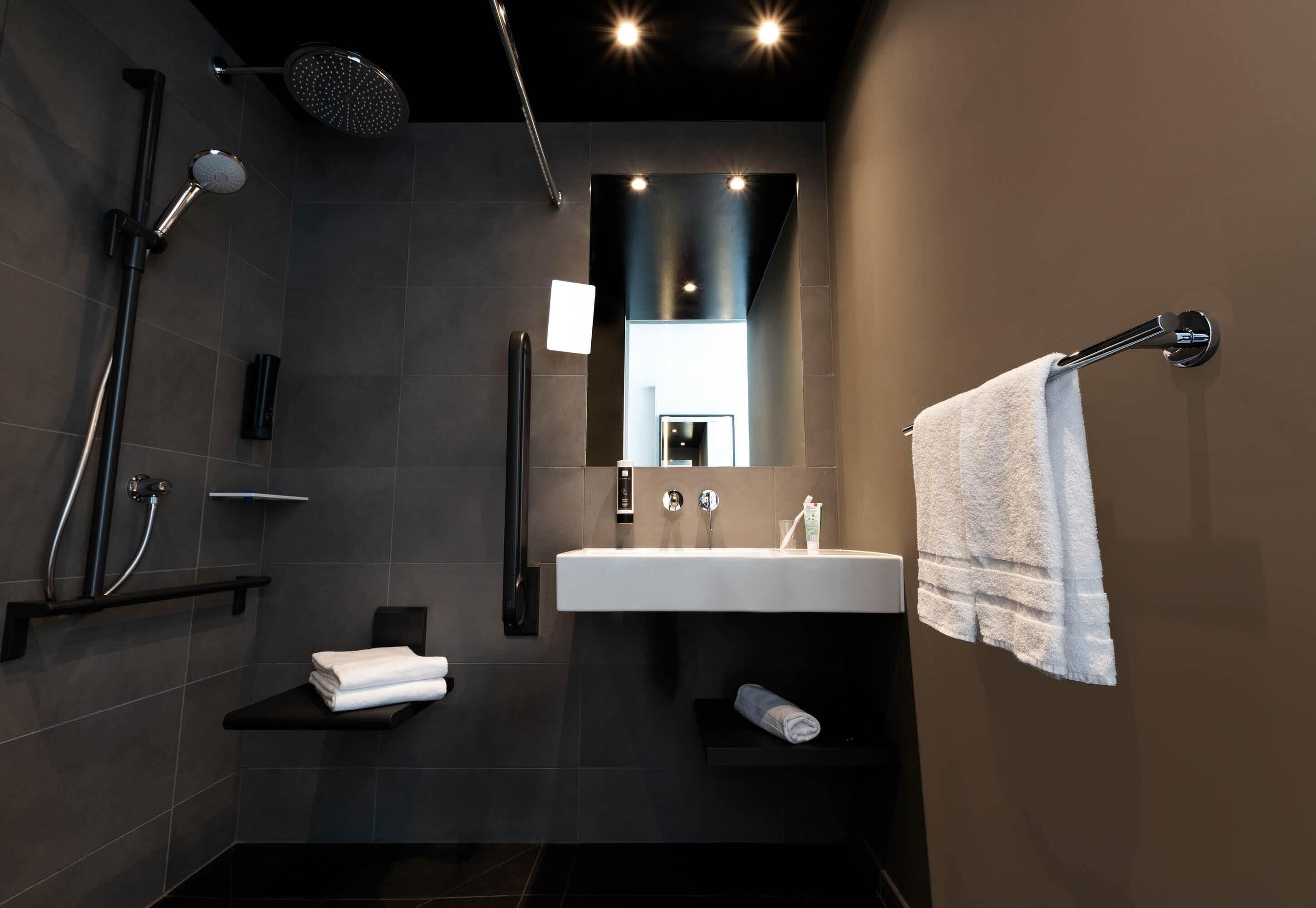 A modern bathroom with a shower, sink, and towel rack.