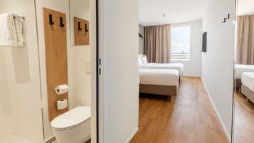 Een hotelkamer met douche, toilet, twee bedden en een groot raam met gordijnen.
