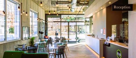 A modern hotel reception area with a reception desk, seating area, and large windows providing natural light.