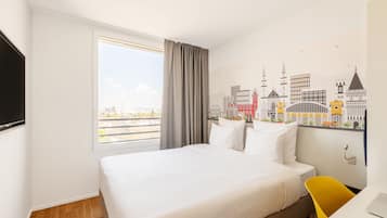 Habitación de hotel con cama, escritorio, silla, televisor y un mural con vista urbana en la pared.