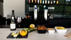 Un bar con una botella de vino, una copa, un shaker de cócteles y diferentes aperitivos.