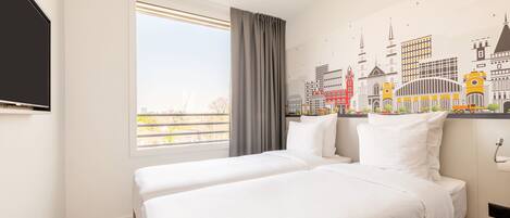 Habitación de hotel con dos camas, un ventanal grande y un mural con vista a la ciudad en la pared.