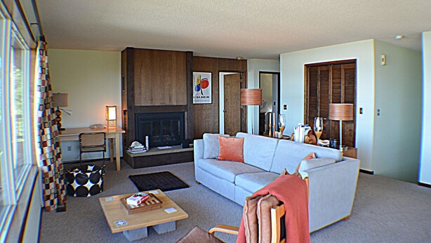 A living room with a fireplace, a sofa, a coffee table, and a bookshelf. - Sea it All - Ocean View Yachats (Yachats)