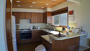 A compact kitchen with wooden cabinets, a stove, a sink, and a window providing natural light. - Sea it All - Ocean View Yachats (Yachats)