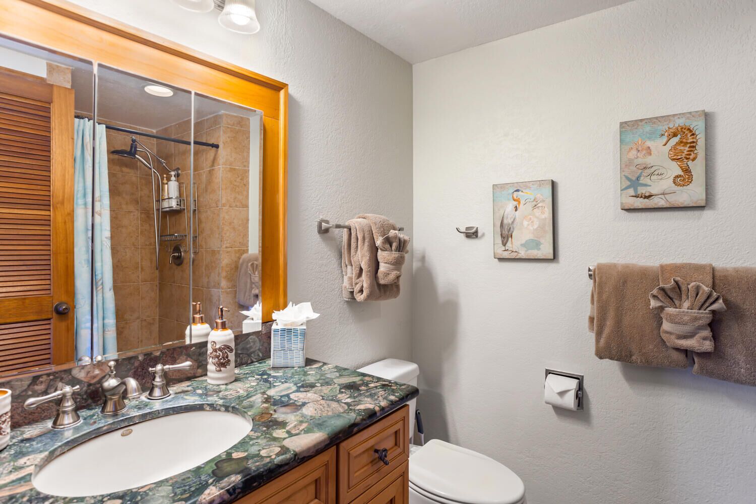 A bathroom with a marble sink, wooden cabinets, a toilet, and a shower with a glass door.