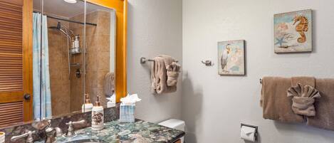 A bathroom with a marble sink, wooden cabinets, a toilet, and a shower with a glass door.