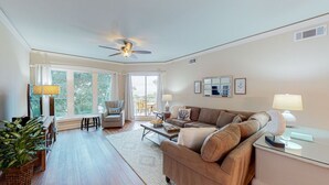 A spacious living room with a large window, a ceiling fan, a sofa, a coffee table, and a side table. - Large Two Bedroom Villa with Ocean Views! (Hilton Head)