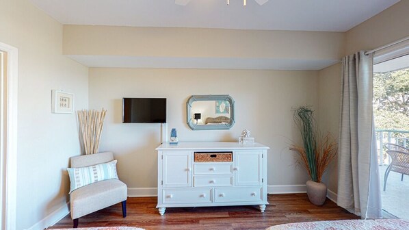 Una habitación con un aparador blanco, un televisor de pantalla plana montado en la pared, una silla con cojines y una planta en maceta.
