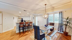 A spacious dining area with a wooden table and chairs, a hanging light fixture, and a view of the kitchen in the background. - Large Two Bedroom Villa with Ocean Views! (Hilton Head)