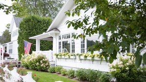 Ett vitt hus med en veranda, ett vitt staket och en trädgård med blommor och buskar.