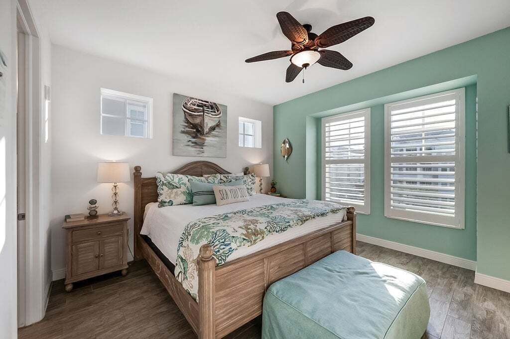A bedroom with a wooden bed, a nightstand, a ceiling fan, and two windows with blinds.