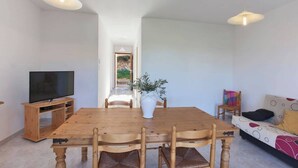 A dining area with a wooden table and chairs, a TV stand, and a sofa with patterned cushions.