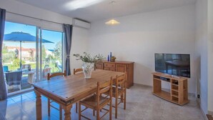 A dining area with a wooden table and chairs, a TV on a wooden stand, and a large window with a view of the outdoors.