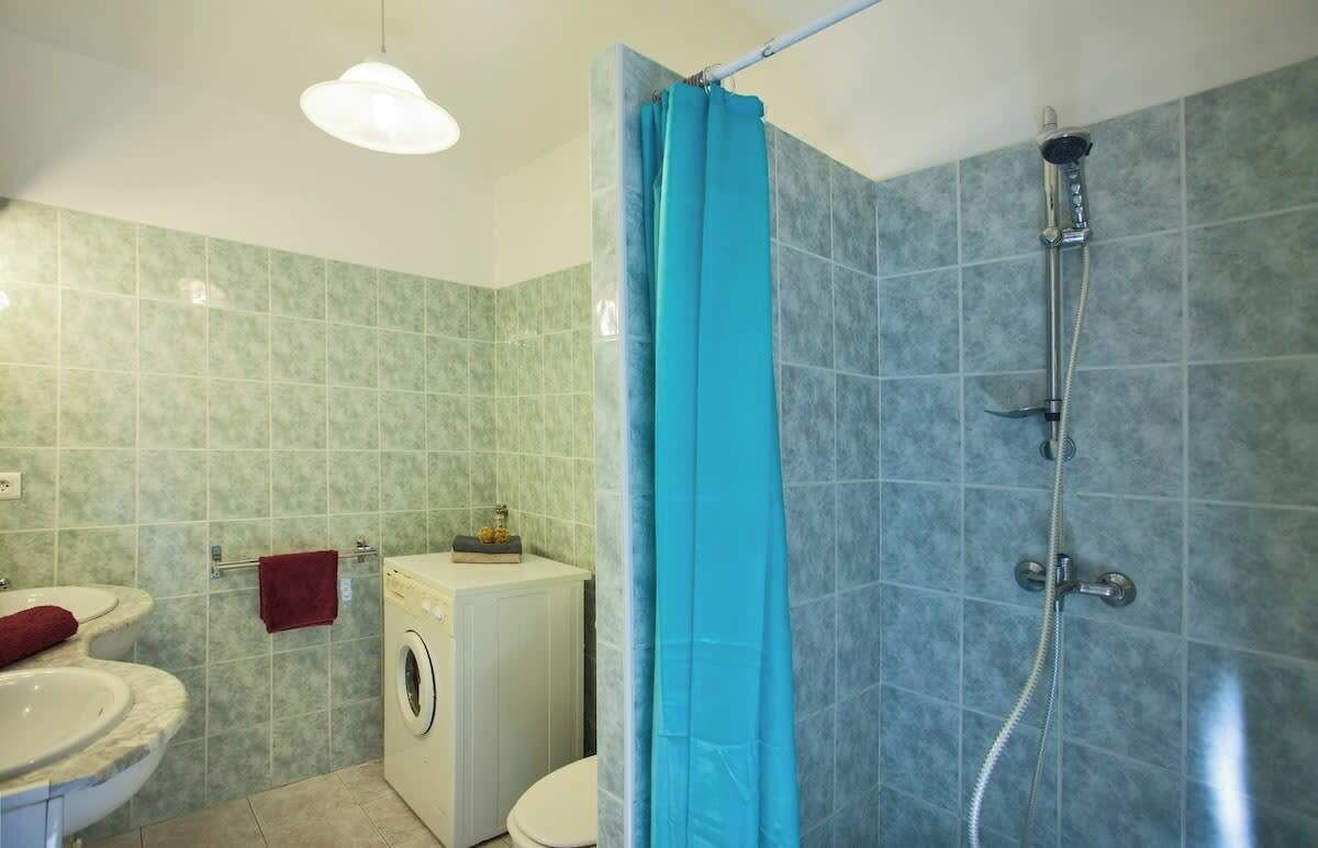 Une salle de bain avec une douche, deux lavabos, des toilettes et un lave-linge.