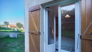 A room with a sliding glass door leading to a balcony, a bed with a white headboard, and a hanging light fixture. - Domaine Bollaccia - Casa Bodri (Monticello)
