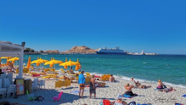 A beach with yellow umbrellas, lounge chairs, and a ship in the background. - Domaine Bollaccia - Casa Bodri (Monticello)