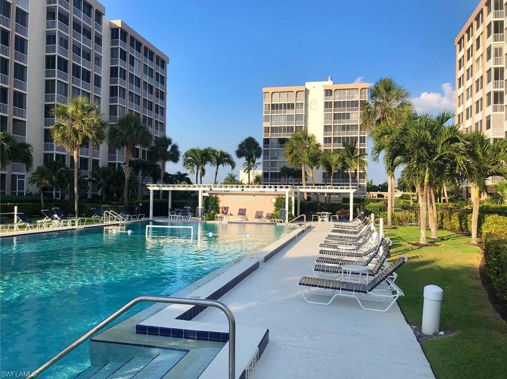 A swimming pool with lounge chairs, palm trees, and high-rise buildings in the background.